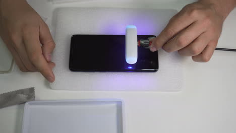 flashlight passes over a smartphone screen to dry the glue