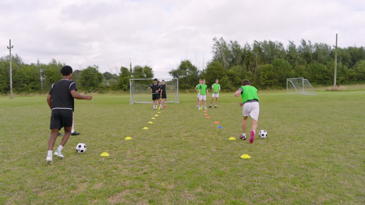Multiracial male soccer players training, running after ball and avoiding obstacles on pitch