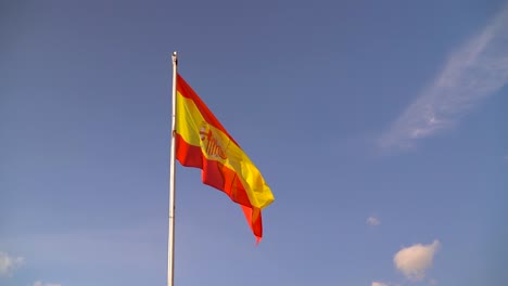 beautiful spanish flag waving against blue sky with few clouds