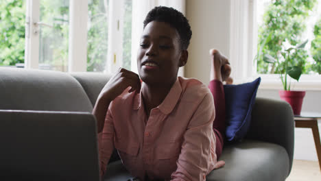 Mujer-Afroamericana-Usando-Una-Computadora-Portátil-Mientras-Está-Acostada-En-El-Sofá-En-Casa