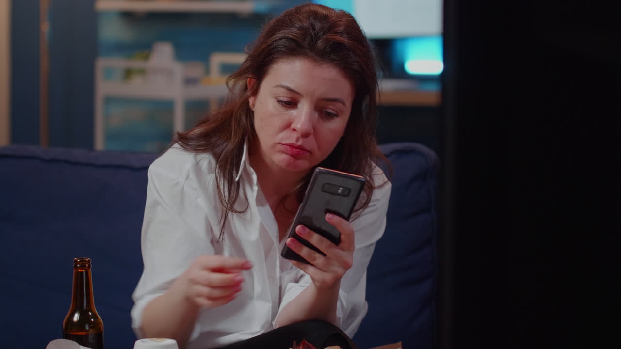 Caucasian woman biting slice of pizza and holding smartphone