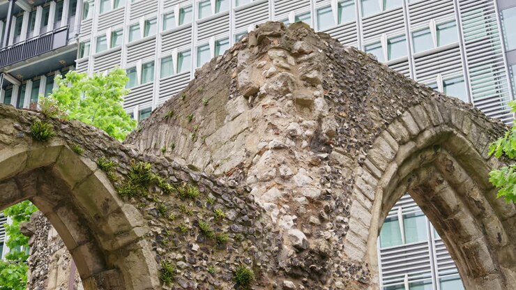 Primo piano di antiche rovine di un muro romano con moderni edifici adibiti a uffici situati nel giardino di London Wall Place