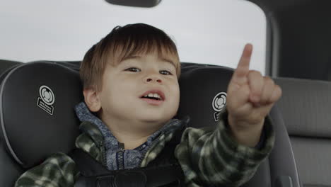 a cheerful two-year-old kid rides in a child car seat, points his fingers forward in front of him