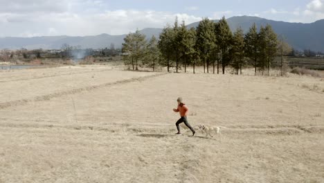 young chinese girl running with dog through remote field in chinese mountains