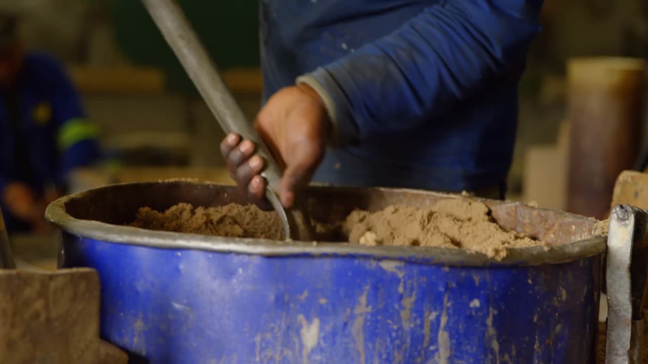 Worker gripping paddle mixing clay for consistency leveling smoothing with charts sliding off frame