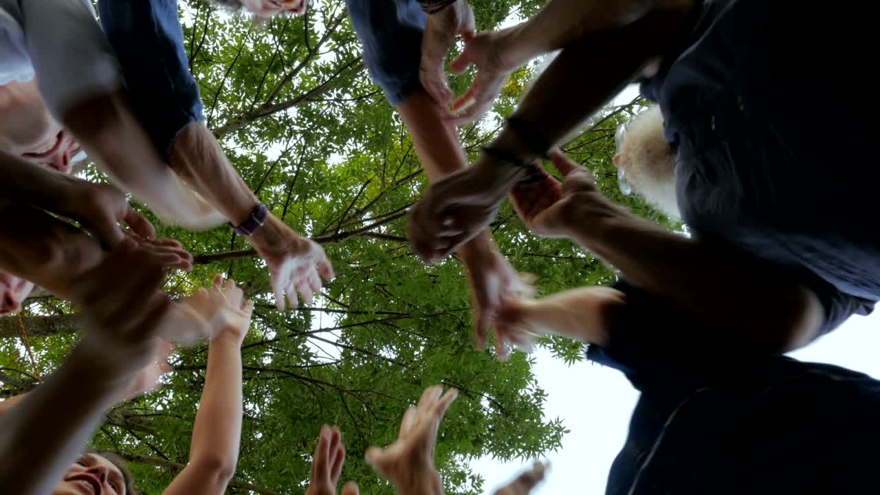 Um grande grupo de pessoas fazendo "high five" juntas em círculo, de várias gerações.