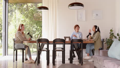recording podcast, diverse female friends sitting at table with microphones and laptops