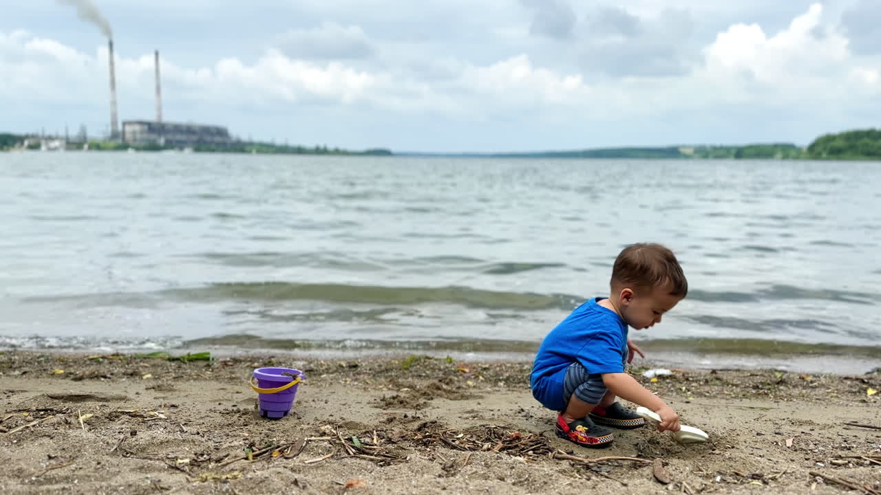 Caucasian child sitting on the beach digging sand with his shovel. Cheerful baby throws the sand at the beach.