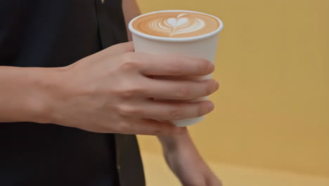 close-up of a hand holding a latte art coffee in a disposable cup