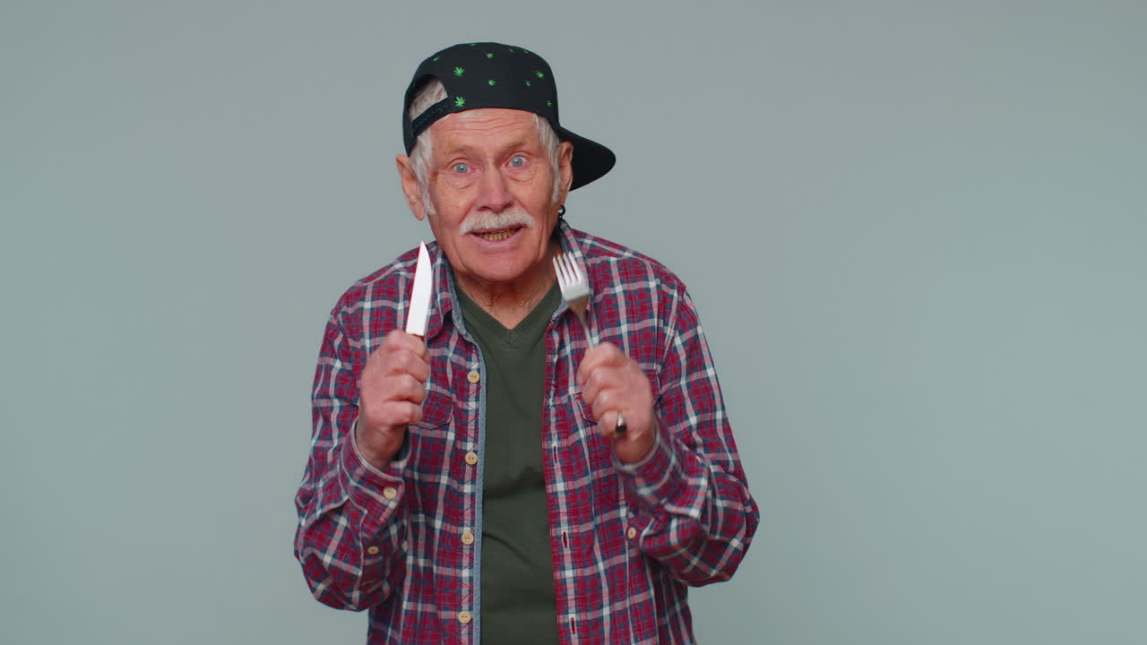 Hungry senior old man waiting for serving dinner dishes with cutlery, will appreciate delicious meal