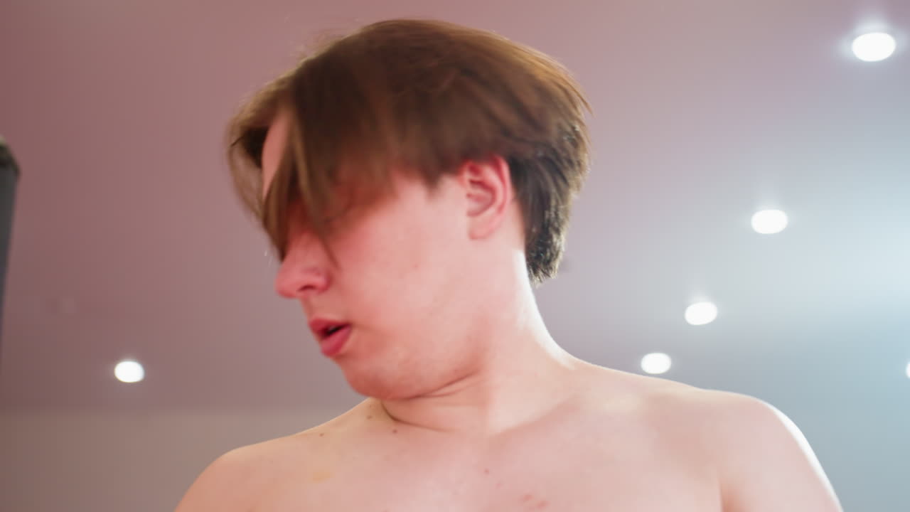 Guy in black turtleneck looks to side with focused expression in gym interior,takes off his shirt soft lighting and punching bag visible in background, creating atmosphere of concentration, discipline, strength