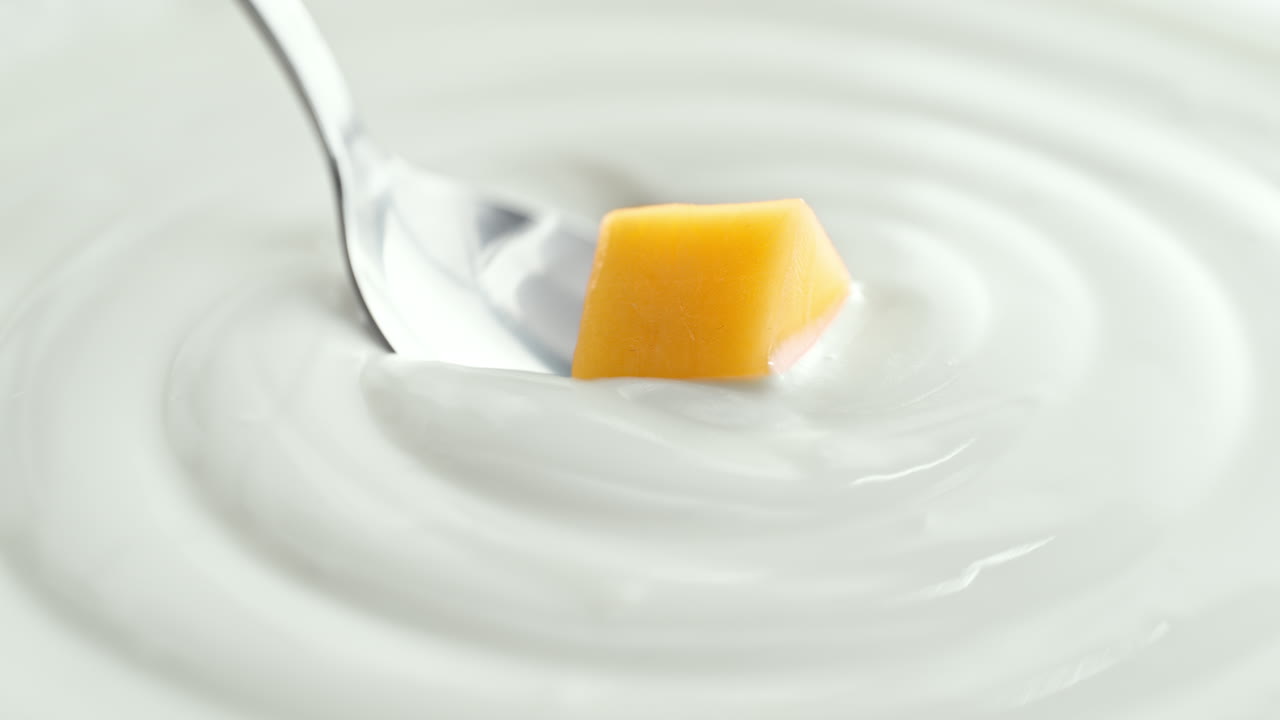 Mango prelevato con un cucchiaio d'argento da yogurt denso e cremoso in macro e slow motion