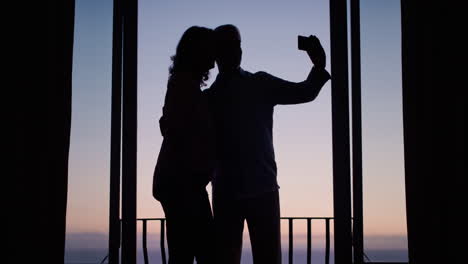 Silhouette-Eines-Glücklichen-Alten-Paares,-Das-Gemeinsam-Mit-Dem-Smartphone-Ein-Foto-Macht-Und-Den-Erfolgreichen-Ruhestand-Bei-Sonnenuntergang-In-Den-Sozialen-Medien-Genießt