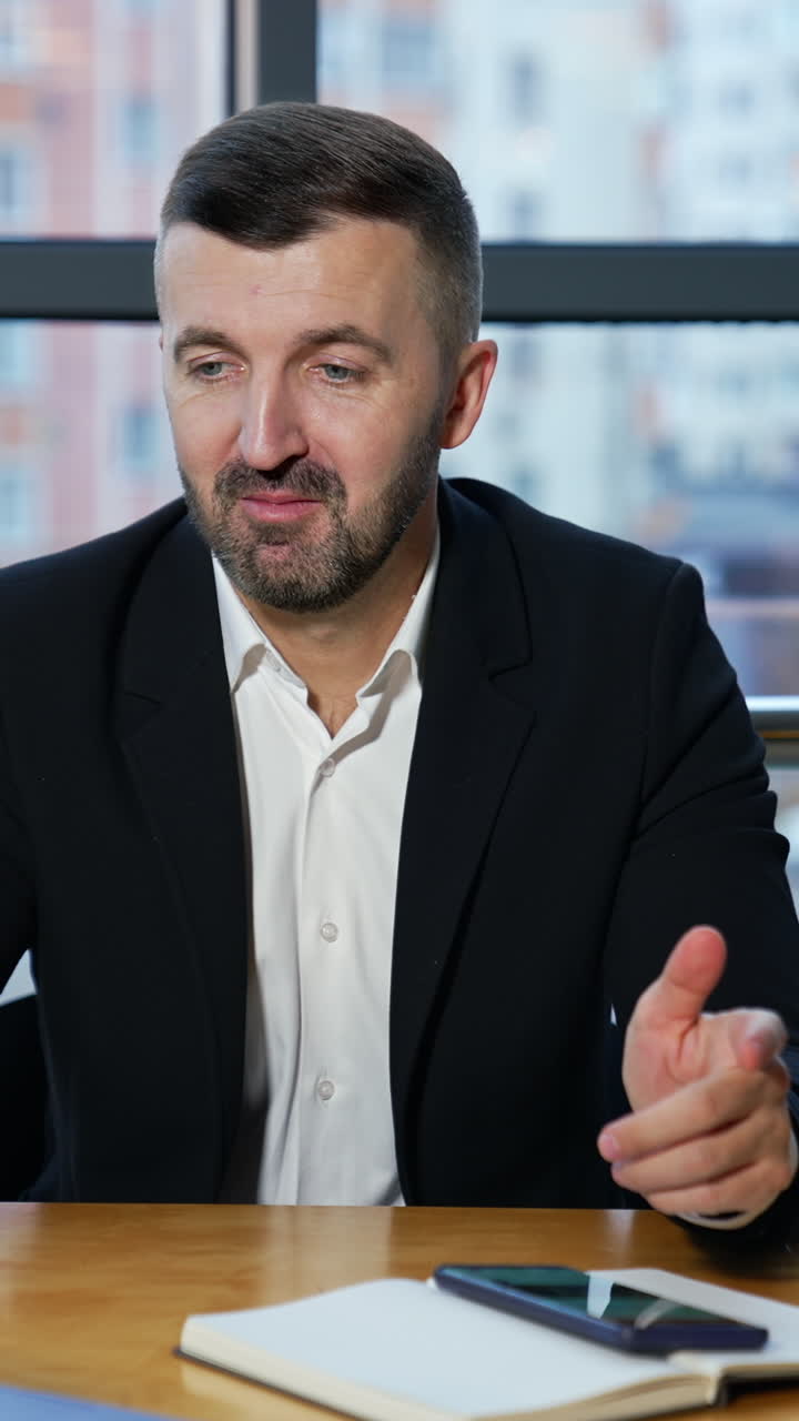 Man in a jacket and suit talk to someone on the laptop and holds a smartphone. Video call to the partners in office. Negotiations via laptop. Vertical video