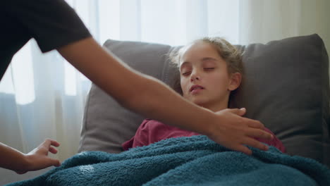 child peacefully sleeping as someone gently covers her with fluffy blanket and checks her temperature by placing hand on her forehead, soft light filters through window