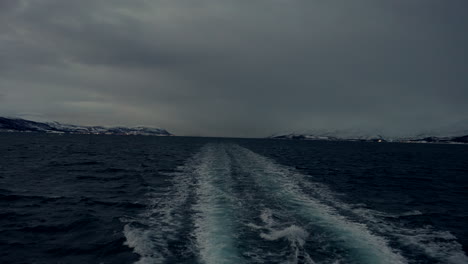 cloudy skies over fjord with wake from cruising boat at dusk in tromso, norway. wide shot