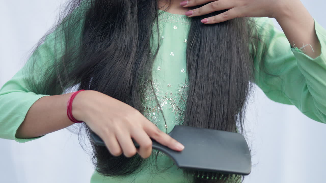 Tight shot of an unrecognisable woman combing her hair with comb in white background, hair care concept.