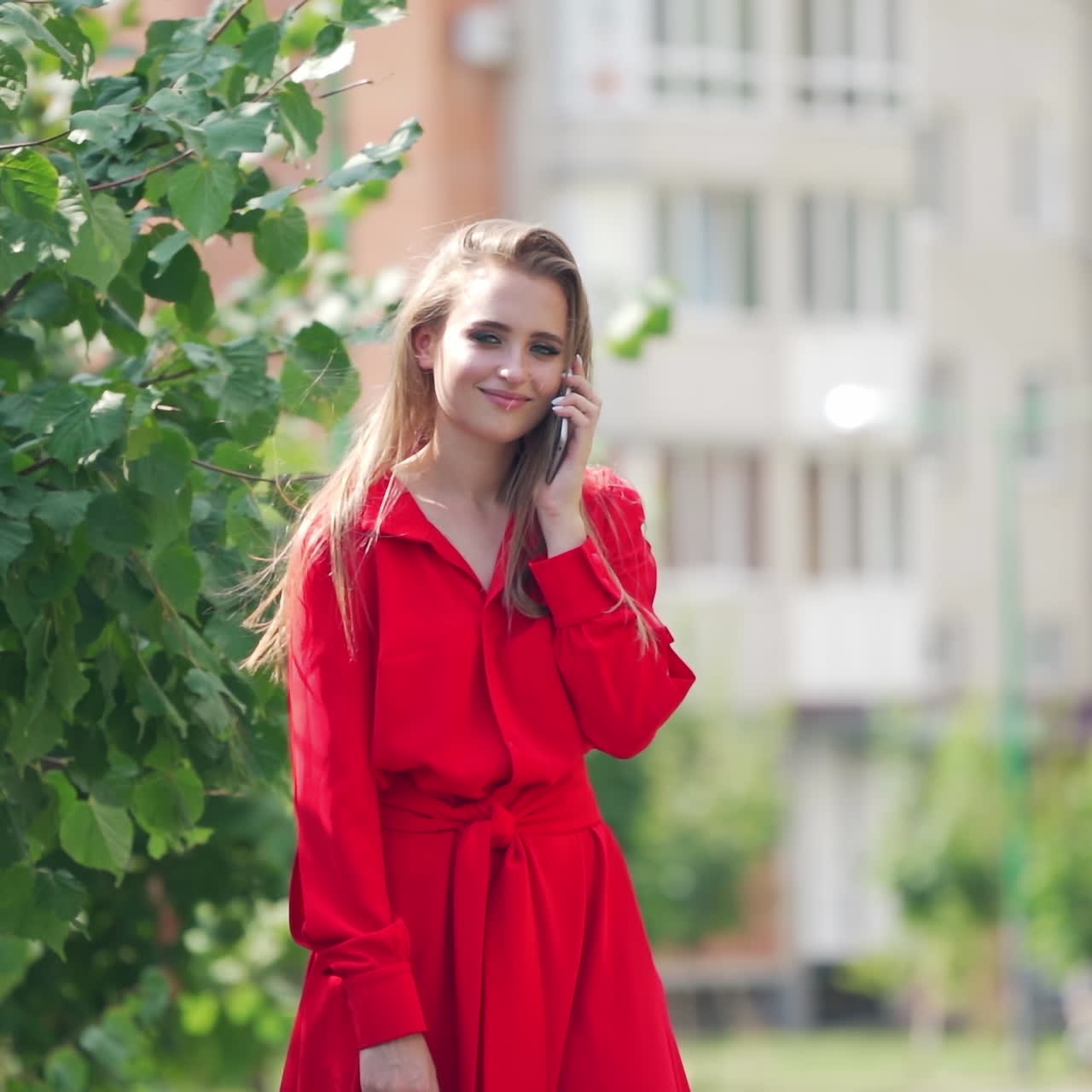 Sad woman in red dress in the city. Beautiful lady holding the mobile phone and becomes happy after calling somebody outdoors. Slow motion.