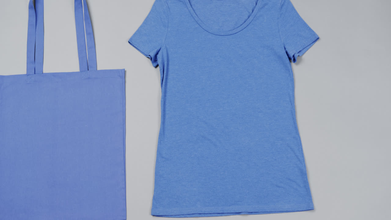 Primo piano di borsa blu e maglietta su sfondo grigio, con spazio per il testo, al rallentatore.