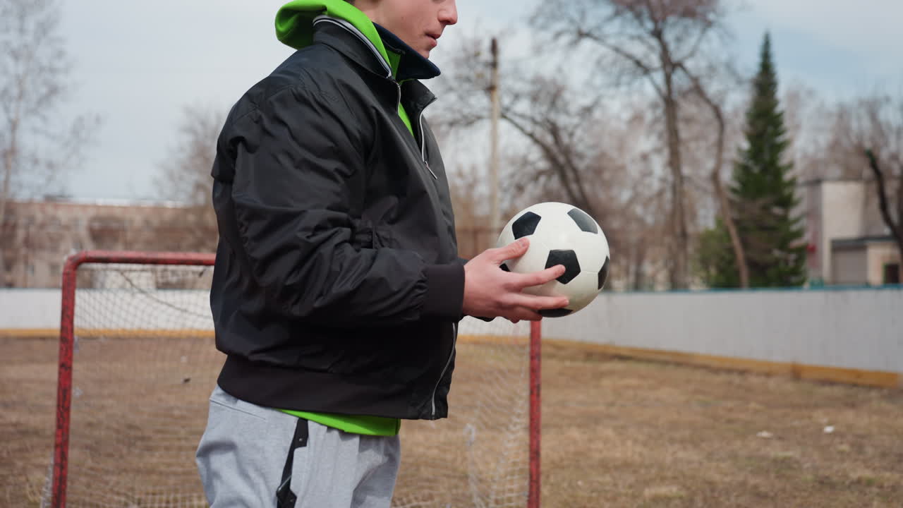야외에서 축구 훈련을 하는 데 집중하는 선수, 오래된 골대 근처에서 축구 연습에 몰두하는 개인, 추운 날씨에 야외 축구 훈련 세션 동안 기술 훈련에 집중하는 운동선수