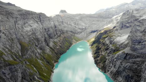 a reverse flyover over a hiker enjoying the view of lake limmernsee in glarus, switzerland, the turquoise colored water of which is surrounded by tall swiss alps peaks and cliffs