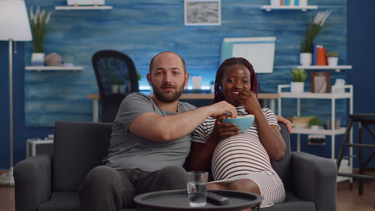 Casal interracial grávido assistindo a um filme na TV