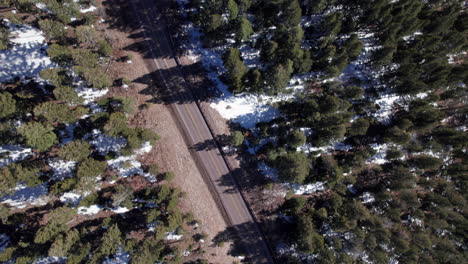 top down view of a snowy mountain road in the forest surrounded by pine trees, drone shot