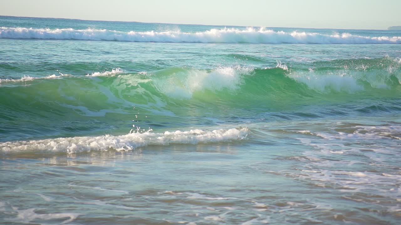 A flawless aqua blue wave breaks in slow motion, curling onto the sand of the Gold Coast’s iconic shoreline in crisp 4K.