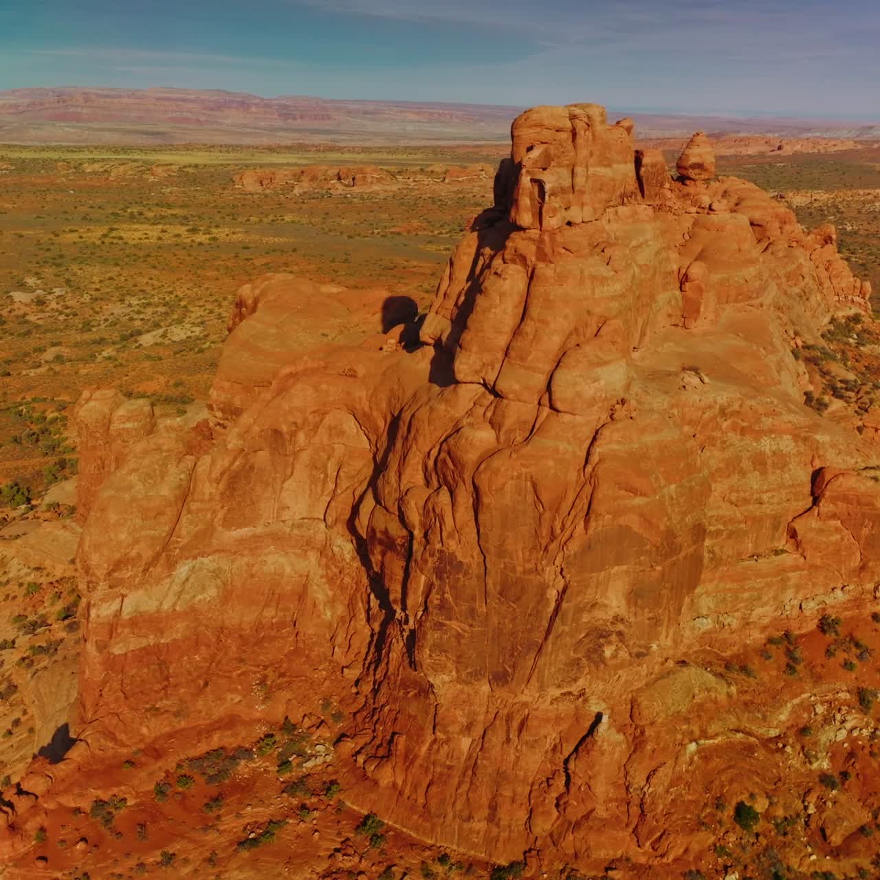 Bright sun lighting the orange mountain. Drone footage around the rock in the deserted landscape. Blue sky at backdrop