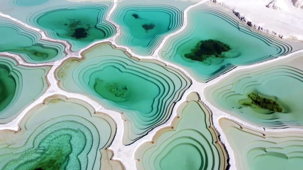 Pemandangan dari atas yang menunjukkan kolam pirus bertingkat yang dipisahkan oleh punggungan mineral putih, pita sedimen krem, tepian melengkung halus, dan pola organik abstrak di seluruh lanskap alam yang tenang