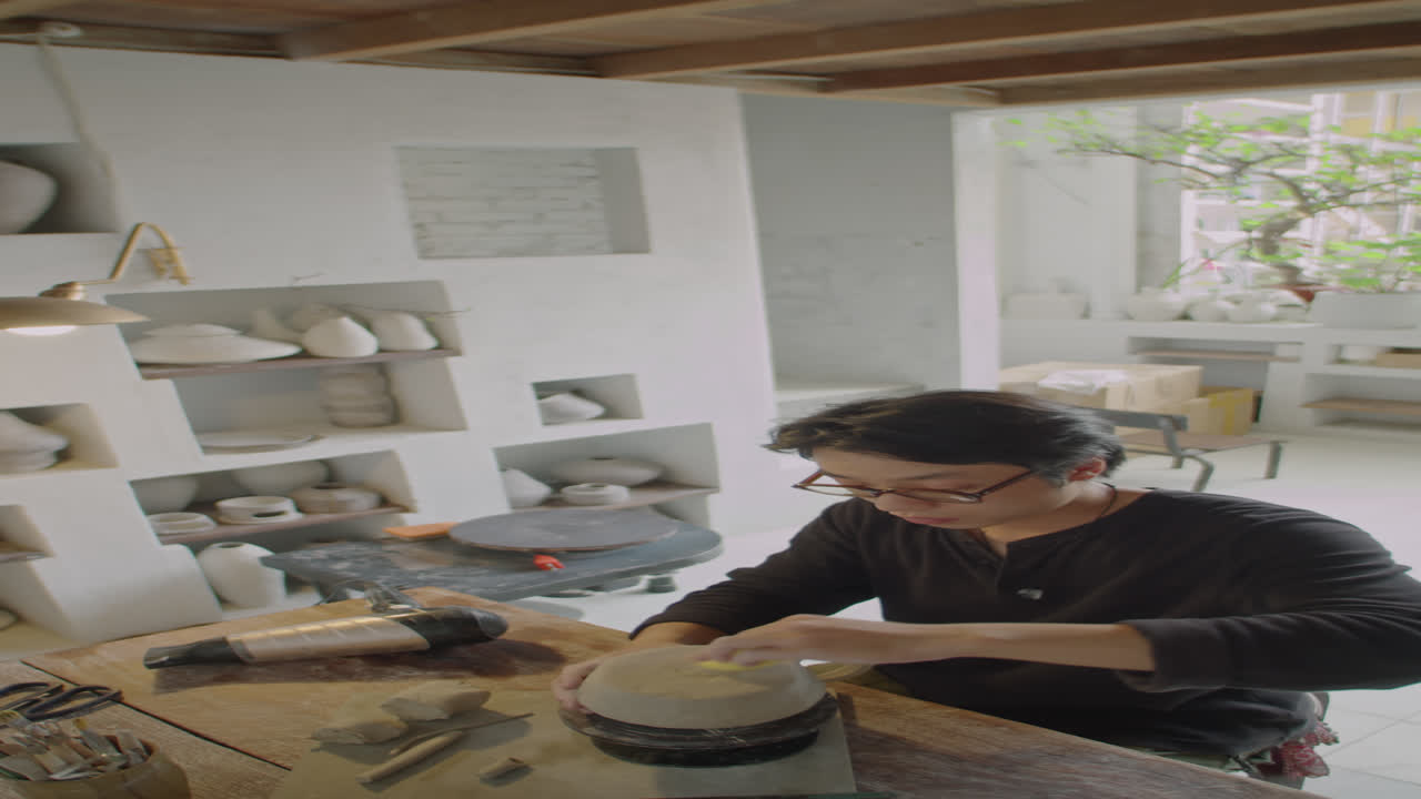 Ceramista che leviga la base di una tazza di argilla in uno studio di ceramica