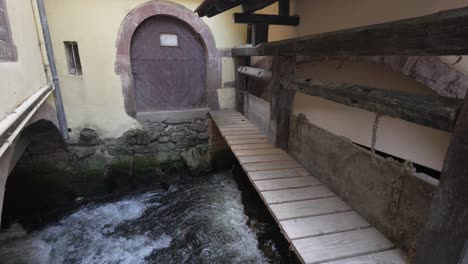 puente panorámico sobre el arroyo hacia la puerta principal de una casa de madera en kaysersberg, francia