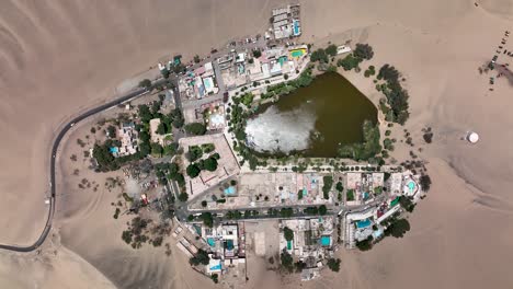 Oasis-Del-Desierto-Huacachina,-Perú-Con-Lago-Y-Palmeras,-Con-Grandes-Dunas-De-Arena-En-El-Fondo