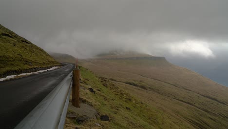 Flying-clouds-between-Hvithamar-cliff-above-Funningur-town-on-Eysturoy-Island-during-dark-cloudy-day---static-wide-shot