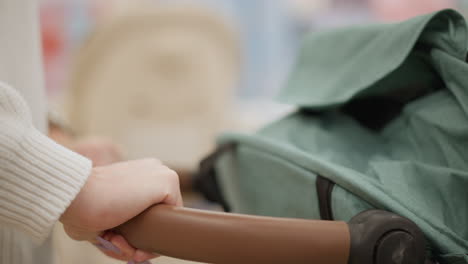 hands of contemplative customer gripping stroller handle, shaking gently to test stability and smooth motion down well lit baby gear aisle inside modern retail store while evaluating quality