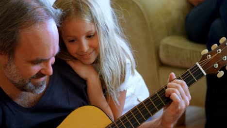 father playing guitar with her daughter in living room 4k