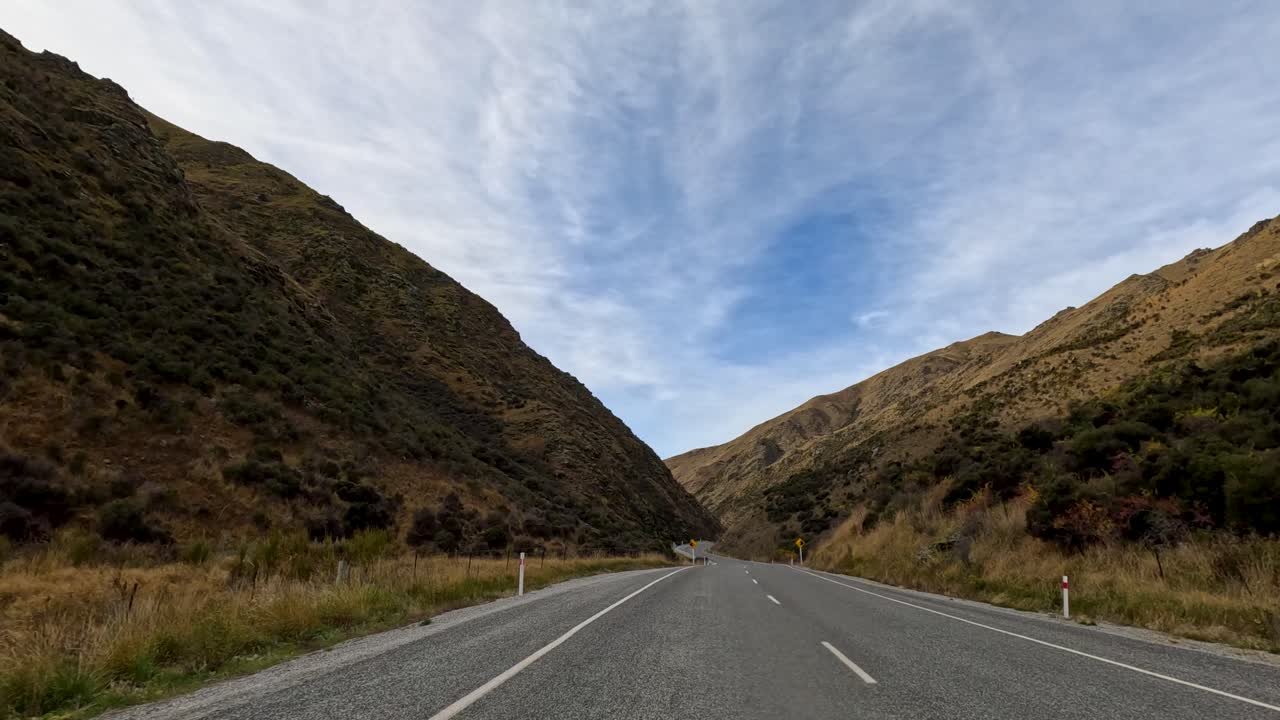 A serene drive through Lake Tekapo's winding roads, surrounded by autumn foliage and mountainous terrain under a vibrant sky