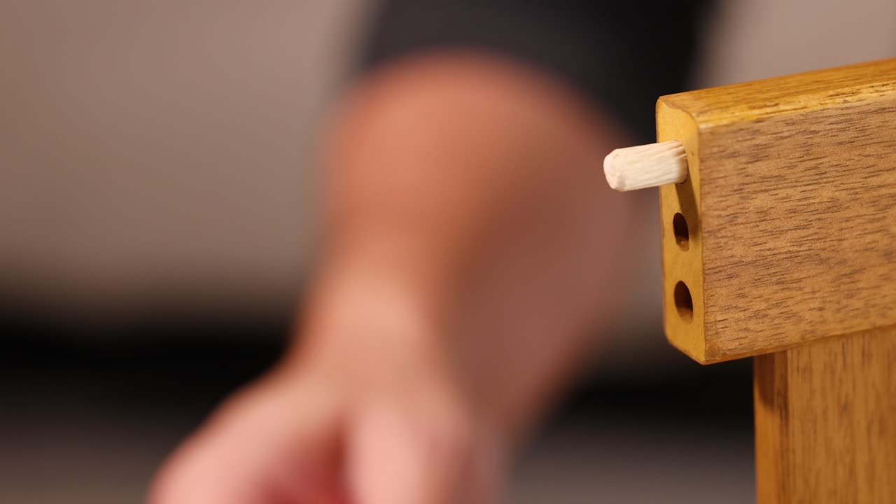 Hands insert a wooden peg into furniture, securing it with a hammer. Close-up shots highlight precision and craftsmanship