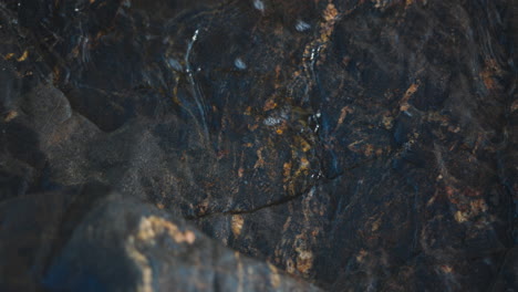 water waves crashing on black rock and polishing its surface