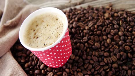 disposable cup with coffee beans on wooden plank