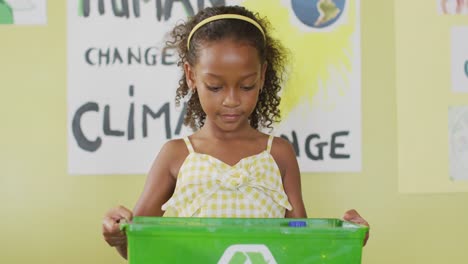 Video-of-happy-african-american-girl-holding-box-with-recycling-symbol-in-classroom