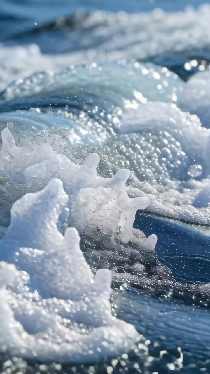 Video verticale: Mareggiata che spinge un'onda illuminata dal sole che si increspa e si infrange vicino alla riva, creando schiuma e spruzzi.