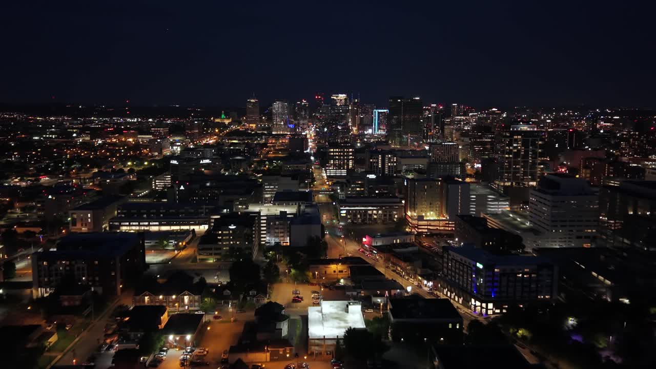 Establishing shot of Nashville, Tennessee skyline at night with glowing lights of a bustling metropolis - forward aerial view