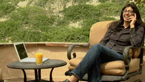 a woman speaks into a cell phone while sitting on a patio 1