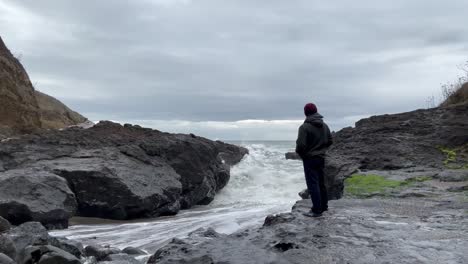 lonely man at the rocky shore with breaking sea waves during cloudy day