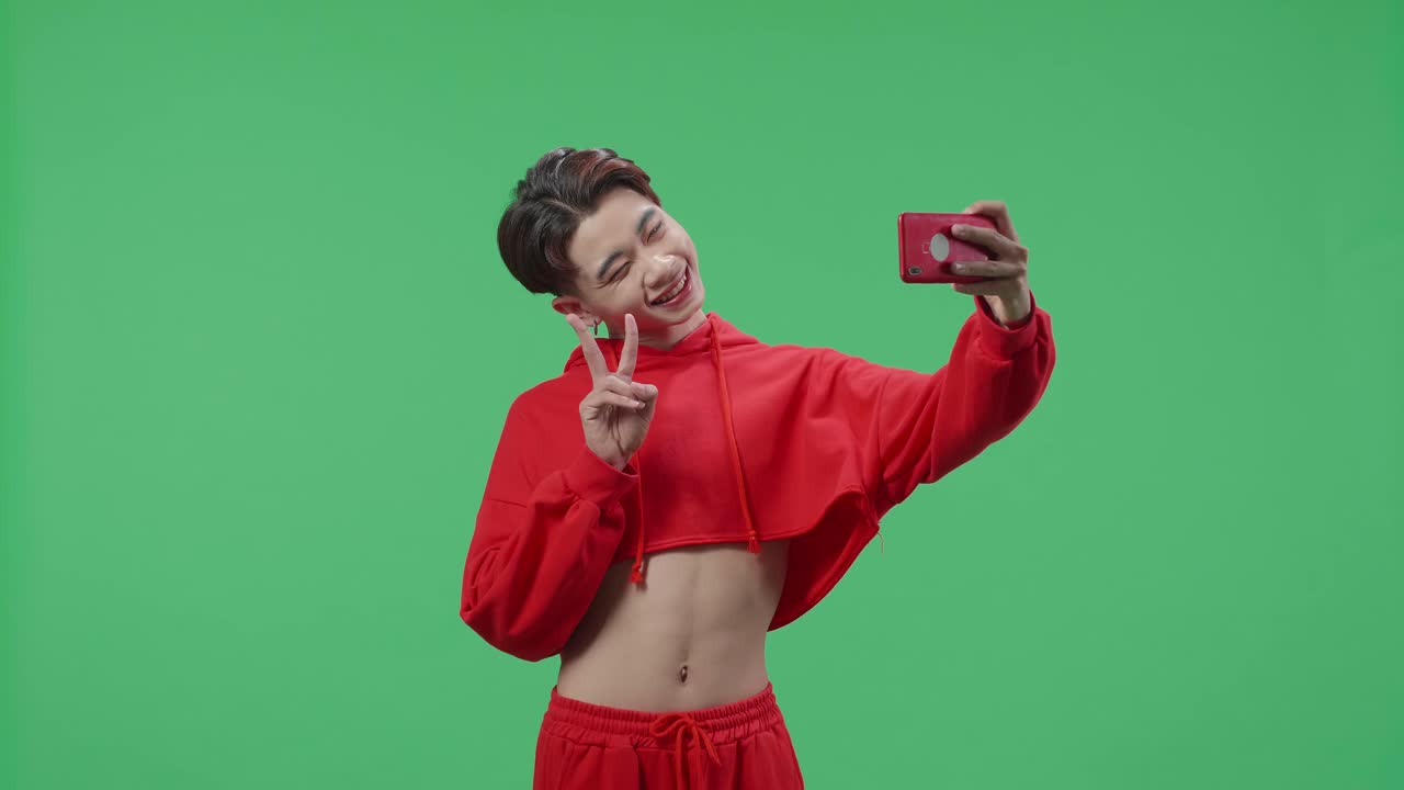 The Smiling Asian Transgender Male Making Selfie While Standing On Green Screen In The Studio