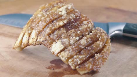 Tiro-Medio-Deslizante-Del-Chicharrón-De-Una-Panceta-Crujiente-Junto-A-Un-Cuchillo-En-Una-Tabla-De-Cortar-De-Madera