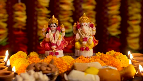 diwali puja preparations with idols of goddess lakshmi and ganesha, a plate of sweets, diyas and dry fruits