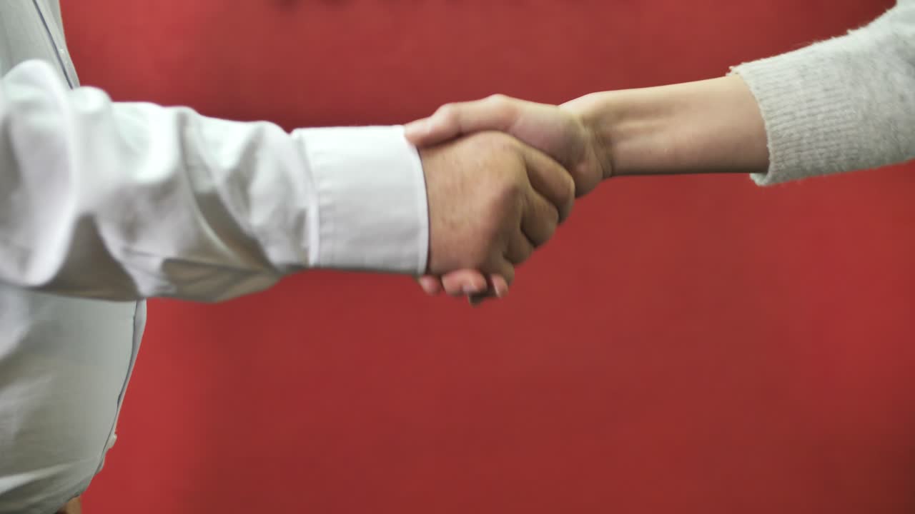 Uomo e donna si stringono la mano professionale su sfondo rosso monocromatico.
