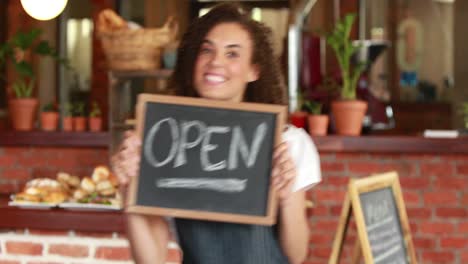 barista sonriente sosteniendo un cartel abierto